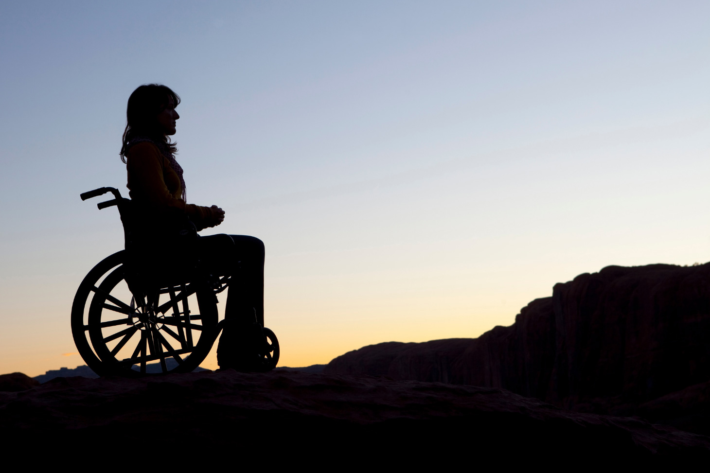 Une étudiante en fauteuil roulant sur un chemin de montagne au coucher de soleil